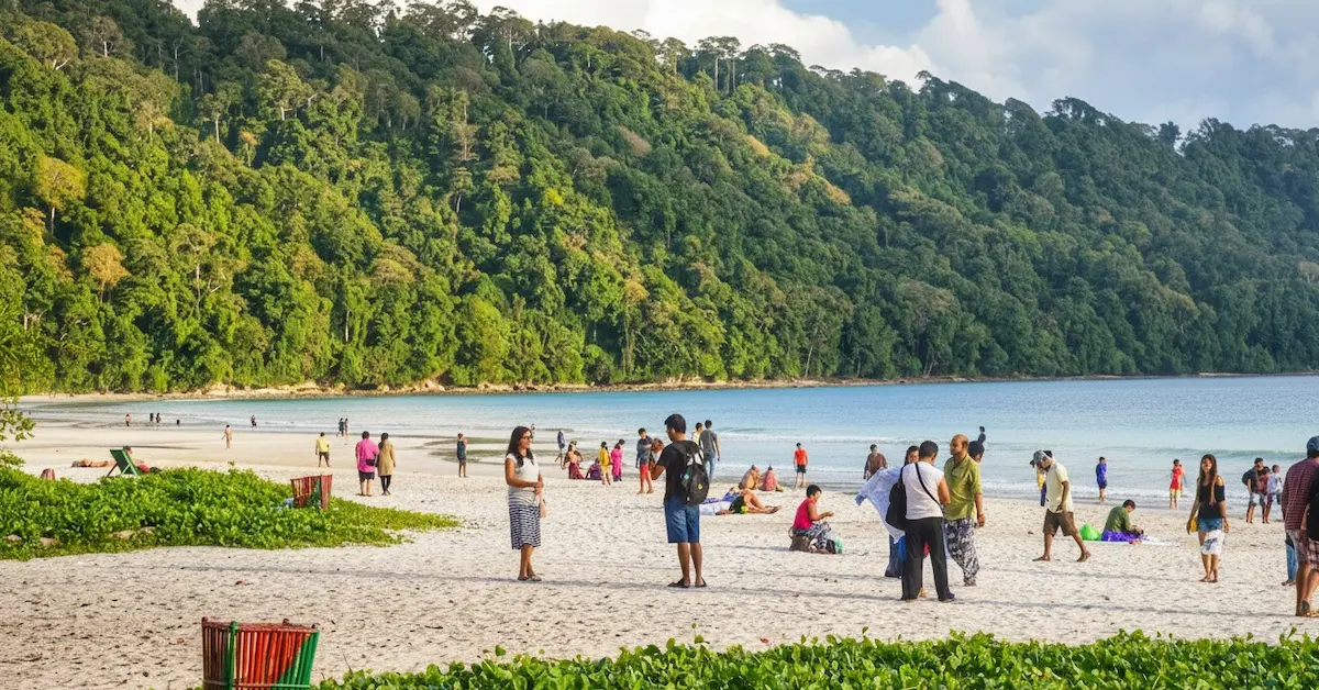 Tourists enjoying Radhanagar Beach in Andaman Islands with white sand, turquoise water, and lush green forest