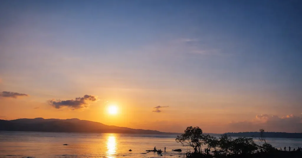 Golden sunset at Chidiya Tapu Beach with calm sea, tree silhouettes, and evening sky in Andaman Islands.