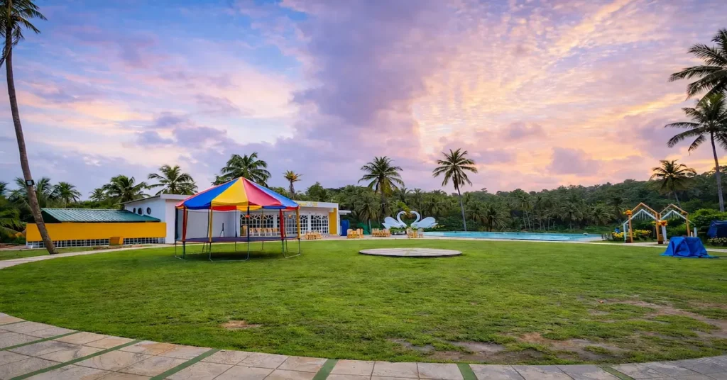 Yellow Garden Port Blair featuring a lush green lawn, palm trees, and a scenic lakeside picnic area.