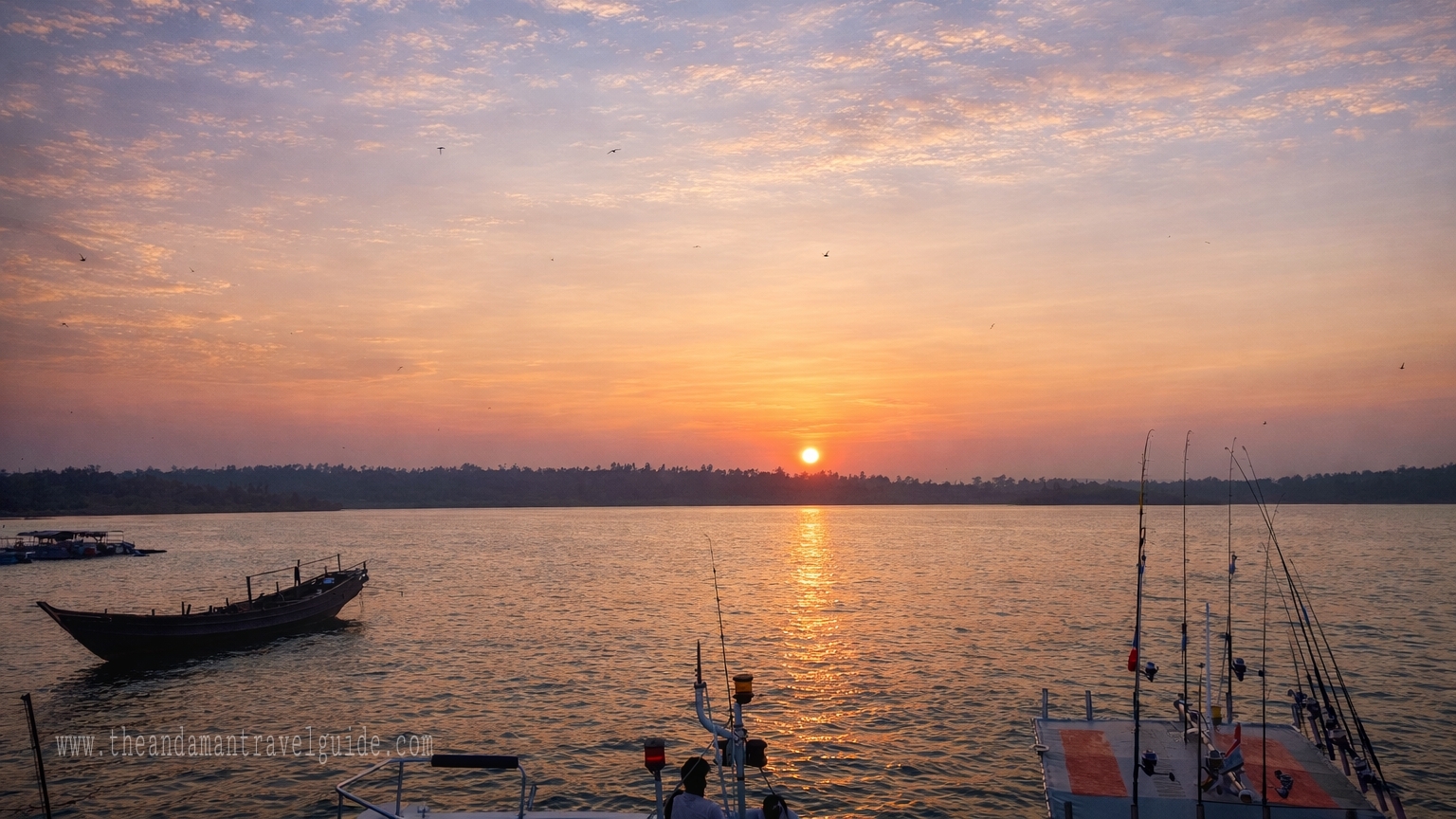 A serene sunset captured from the Aerial Bay Jetty. The sun is a bright orange orb near the horizon, casting a shimmering golden reflection across the calm sea.