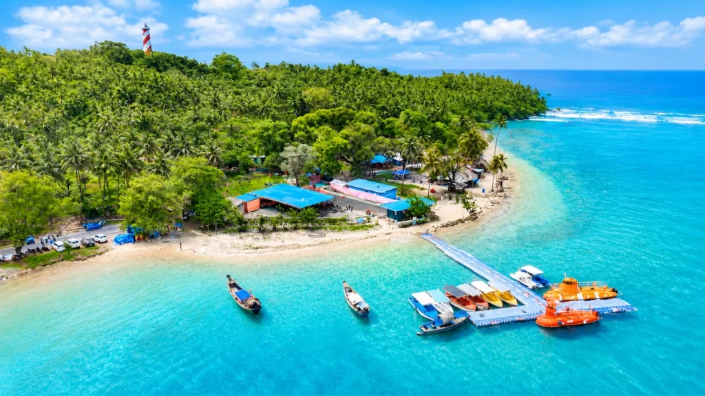 Aerial view of North Bay Island Andaman featuring the iconic red and white lighthouse, crystal-clear turquoise waters, and speedboats docked at the floating jetty.