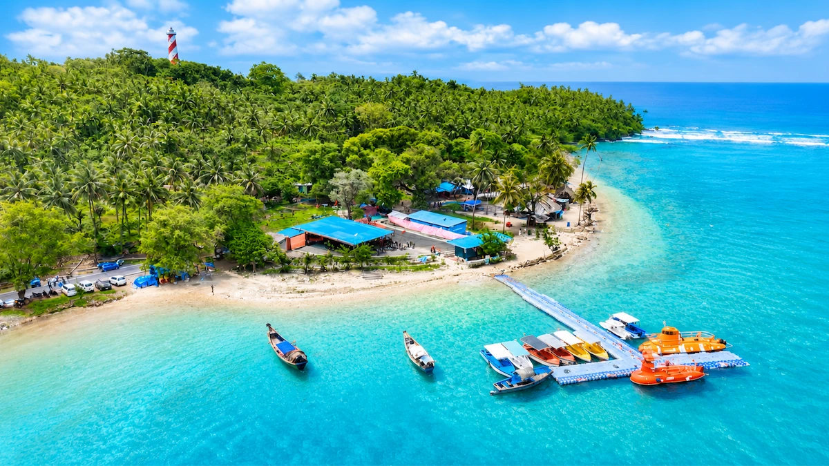 Aerial view of North Bay Island Andaman featuring the iconic red and white lighthouse, crystal-clear turquoise waters, and speedboats docked at the floating jetty.