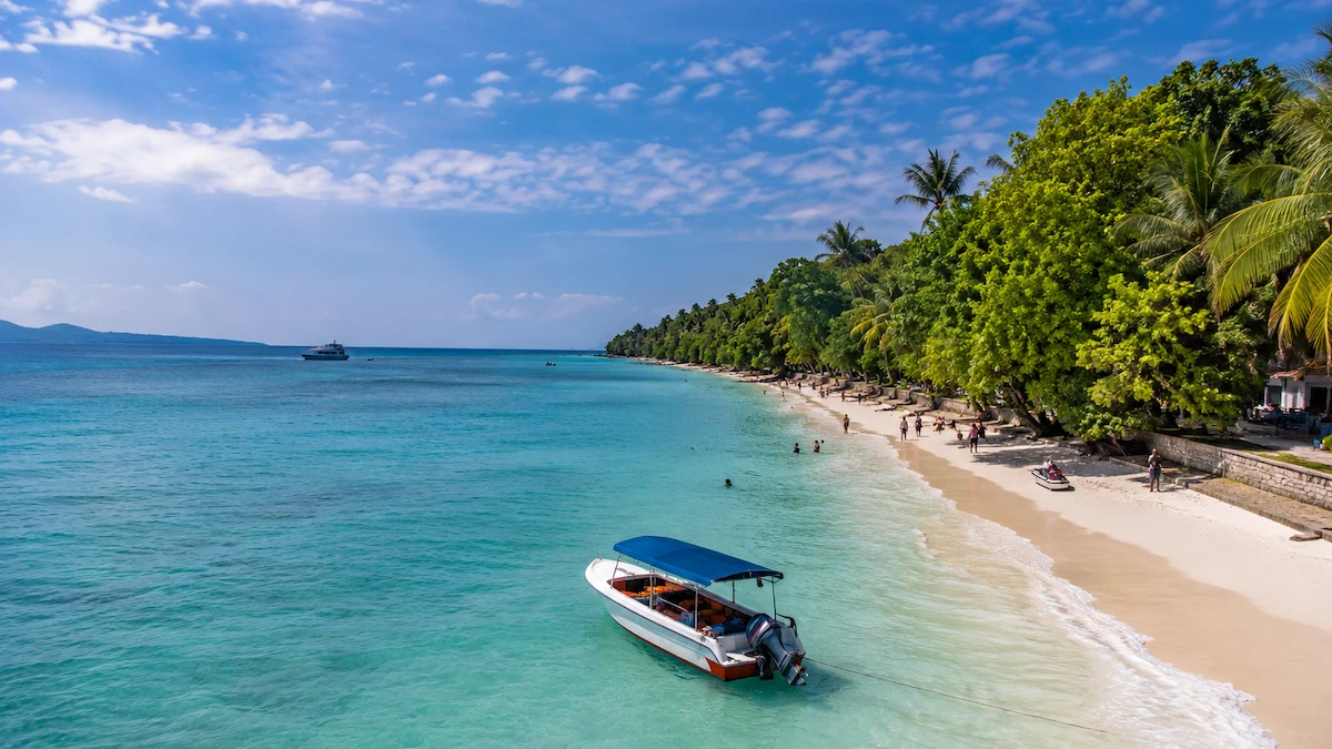 Tourists enjoying a beautiful beach in the Andaman Islands with turquoise water, white sand, palm trees, and water activities.