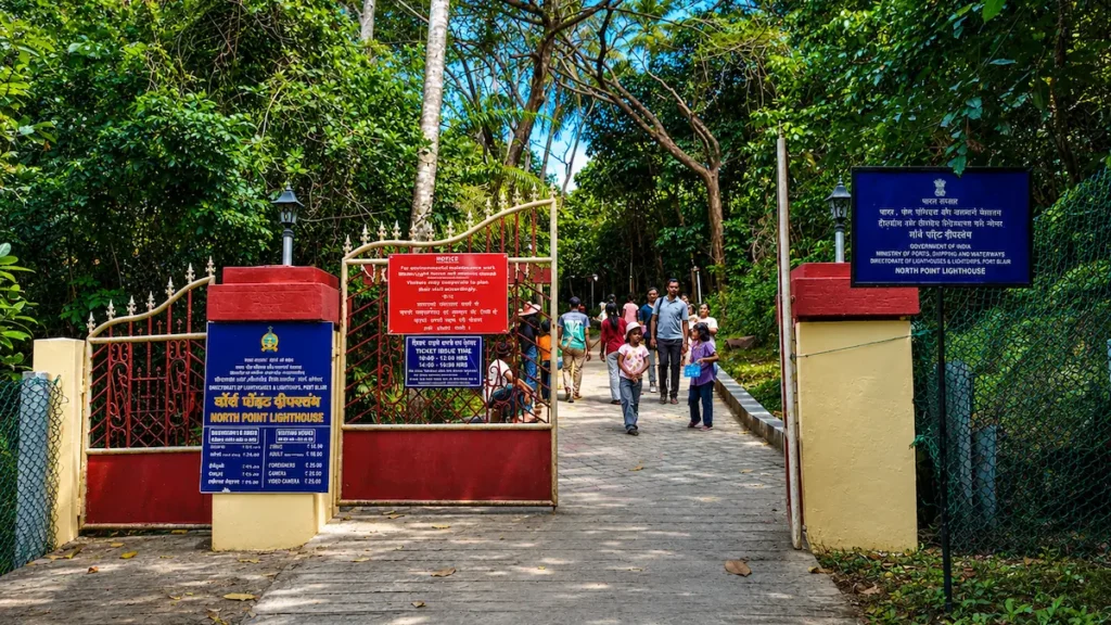 North Bay Island Andaman lighthouse entrance gate showing the ticket counter boards and the paved hill footpath where tourists are walking up to the lighthouse.