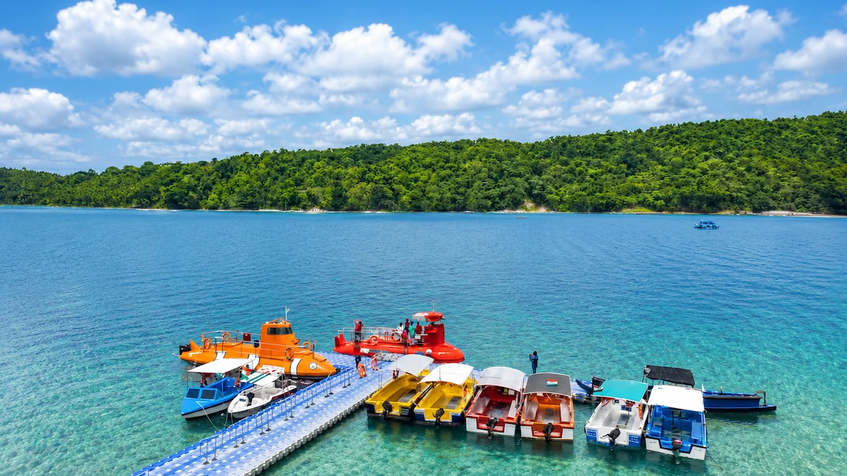 North Bay Island Andaman floating jetty with colorful speedboats and semi-submarine rides docked in crystal-clear blue waters against a lush green hill background.
