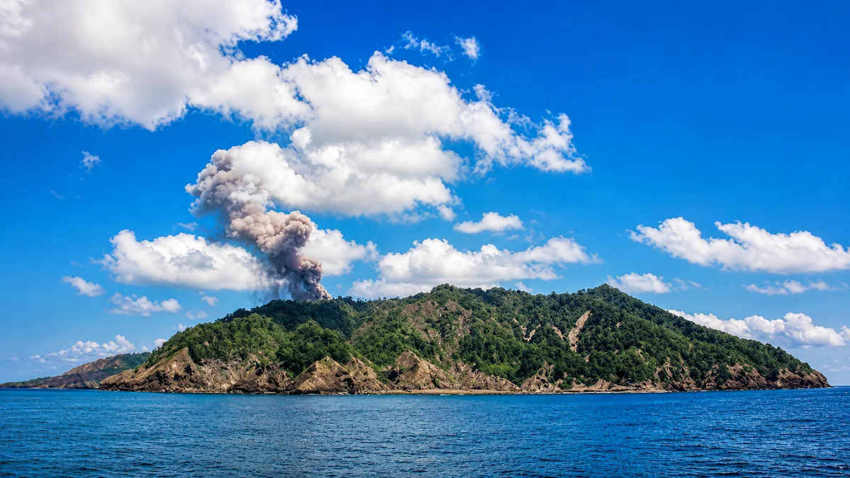 Barren Island, India's only active volcano, seen from the sea with volcanic smoke rising above the lush green island in the Andaman and Nicobar Islands.