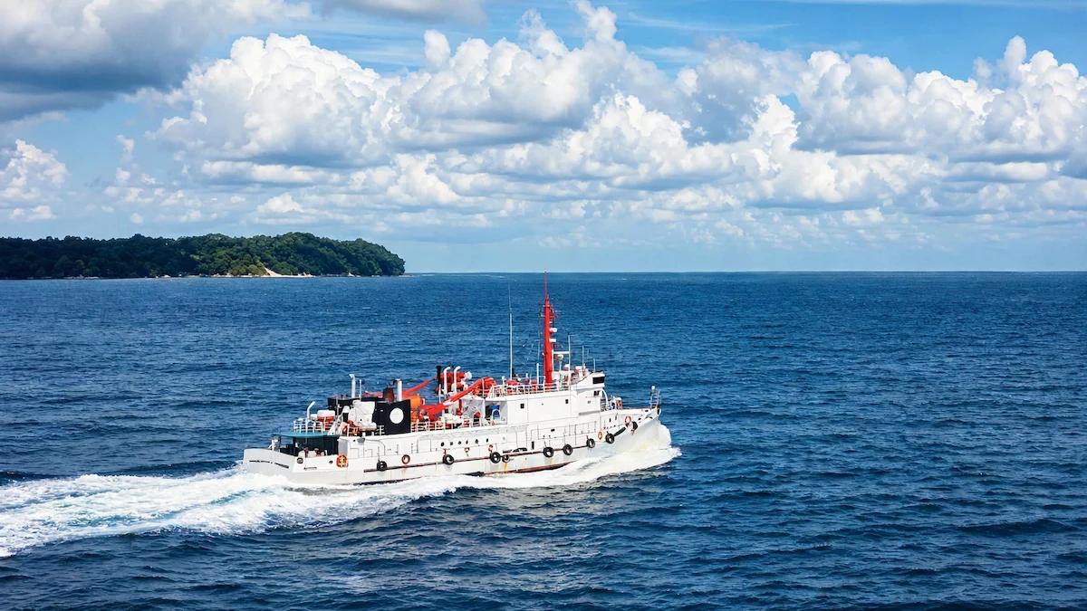 Neil Island: The Perfect Escape from Crowded Island Life Government ferry cruising towards Neil Island (Shaheed Dweep) in Andaman, sailing on deep blue sea with cloudy sky and green island in background.