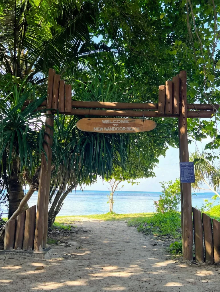 Wooden entrance gate at Wandoor Beach in South Andaman surrounded by tropical trees with the sea visible in the background.